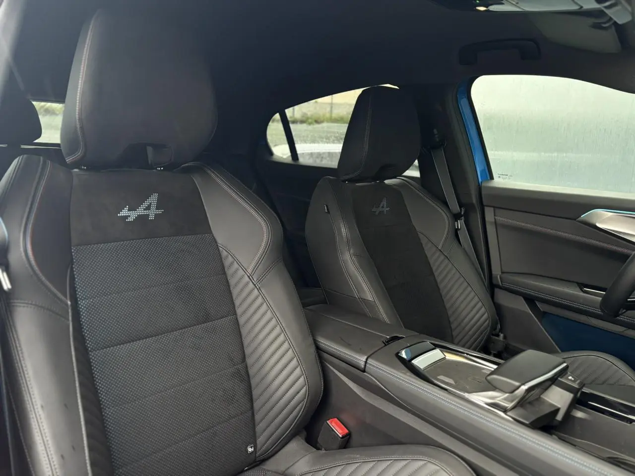 Vue intérieure côté droit montrant les sièges avant noirs avec logo Alpine brodé et surpiqûres contrastées.