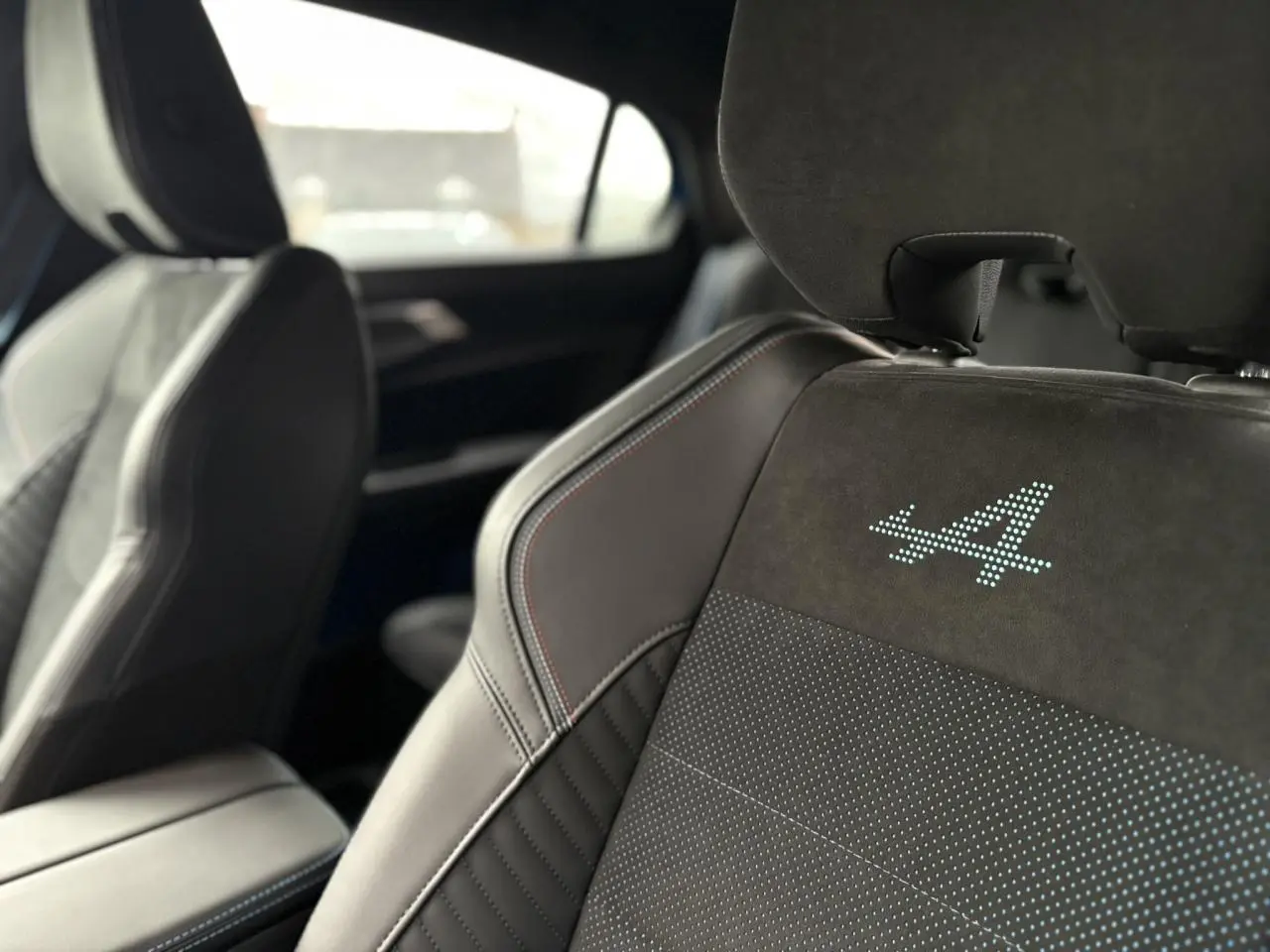 Gros plan sur les sièges avant en Alcantara noir avec surpiqûres tricolores et logo « A » lumineux du Renault Rafale.