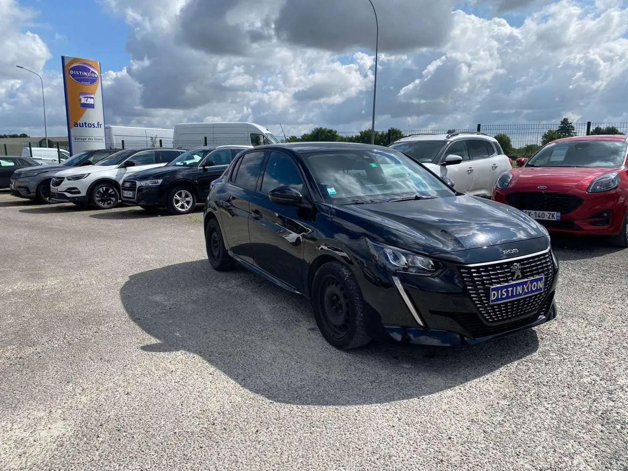 Peugeot 208 noire vue en 3/4 avant droit sur parking, avec calandre distinctive et plaque Distinxion.