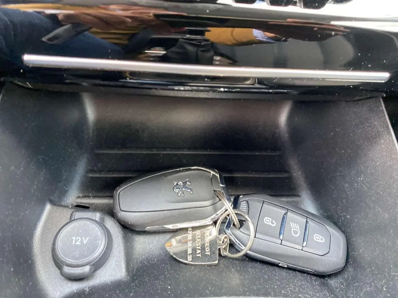 Gros plan sur les clés Peugeot posées dans la console centrale noire d'une 208 Essence 2021, avec prise 12V visible.