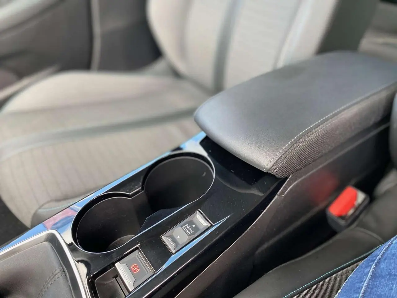 Gros plan sur la console centrale noire de la Peugeot 208 Allure 2021 avec accoudoir et boutons de frein à main électrique.