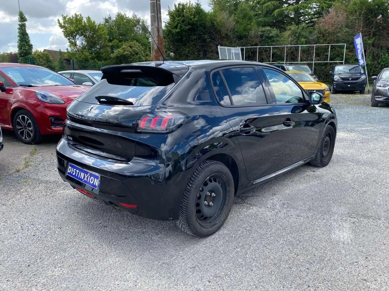 Vue 3/4 arrière droite d'une Peugeot 208 noire 2021 avec jantes tôles et feux arrière à griffes rouges.
