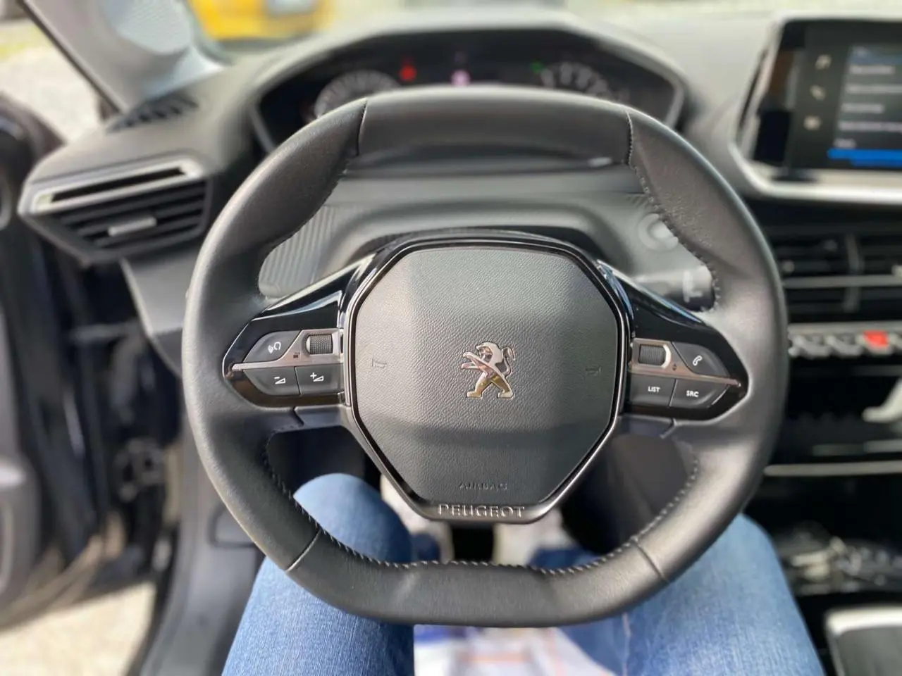 Vue rapprochée du volant noir de la Peugeot 208 2021 avec commandes intégrées et tableau de bord en arrière-plan.