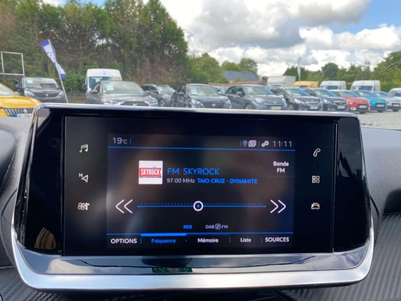 Écran tactile central de la Peugeot 208 noire de 2021 affichant la radio FM Skyrock en intérieur véhicule.