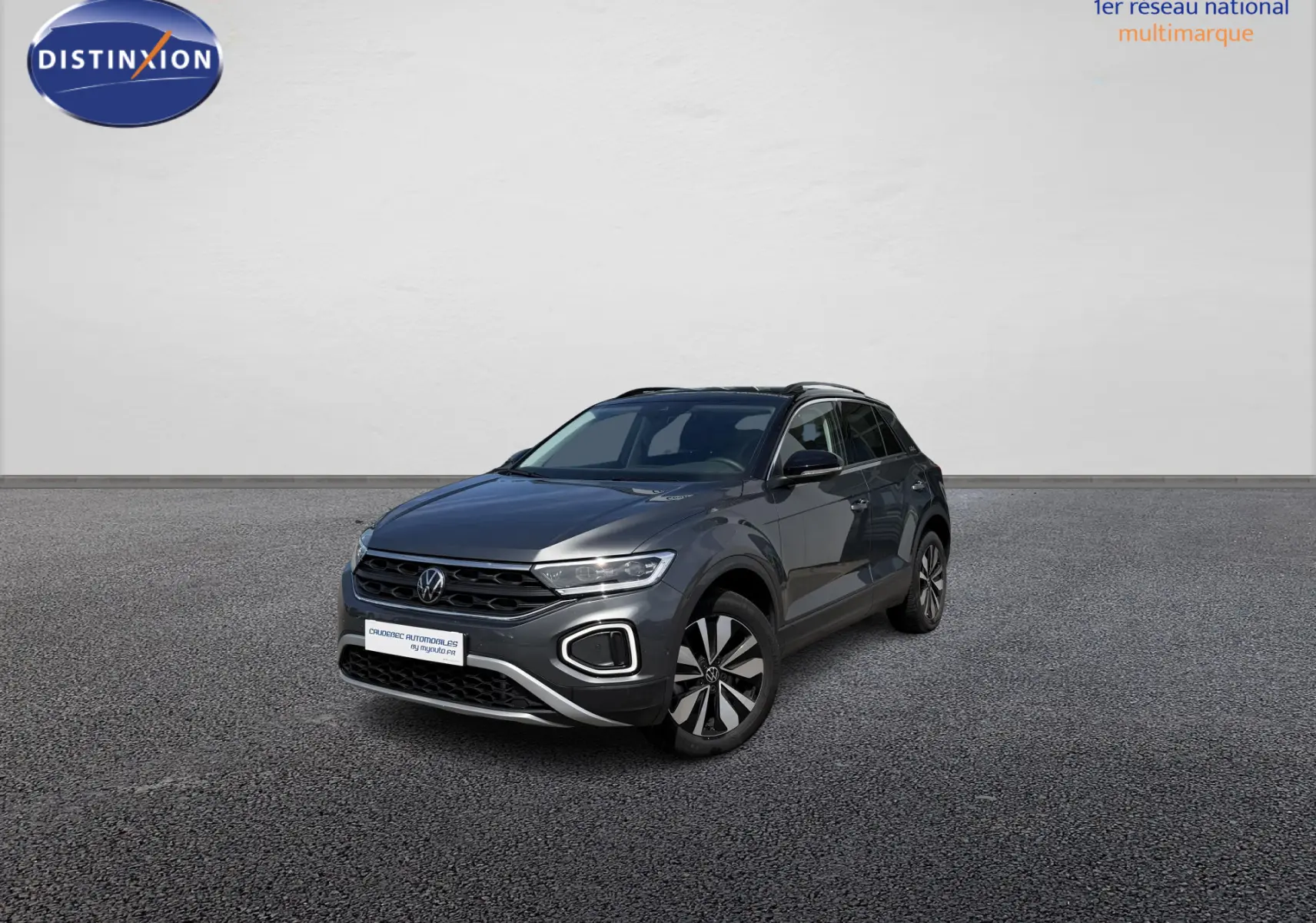 Volkswagen T-Roc gris en 3/4 avant droit, avec barres de toit noires et jantes distinctives.