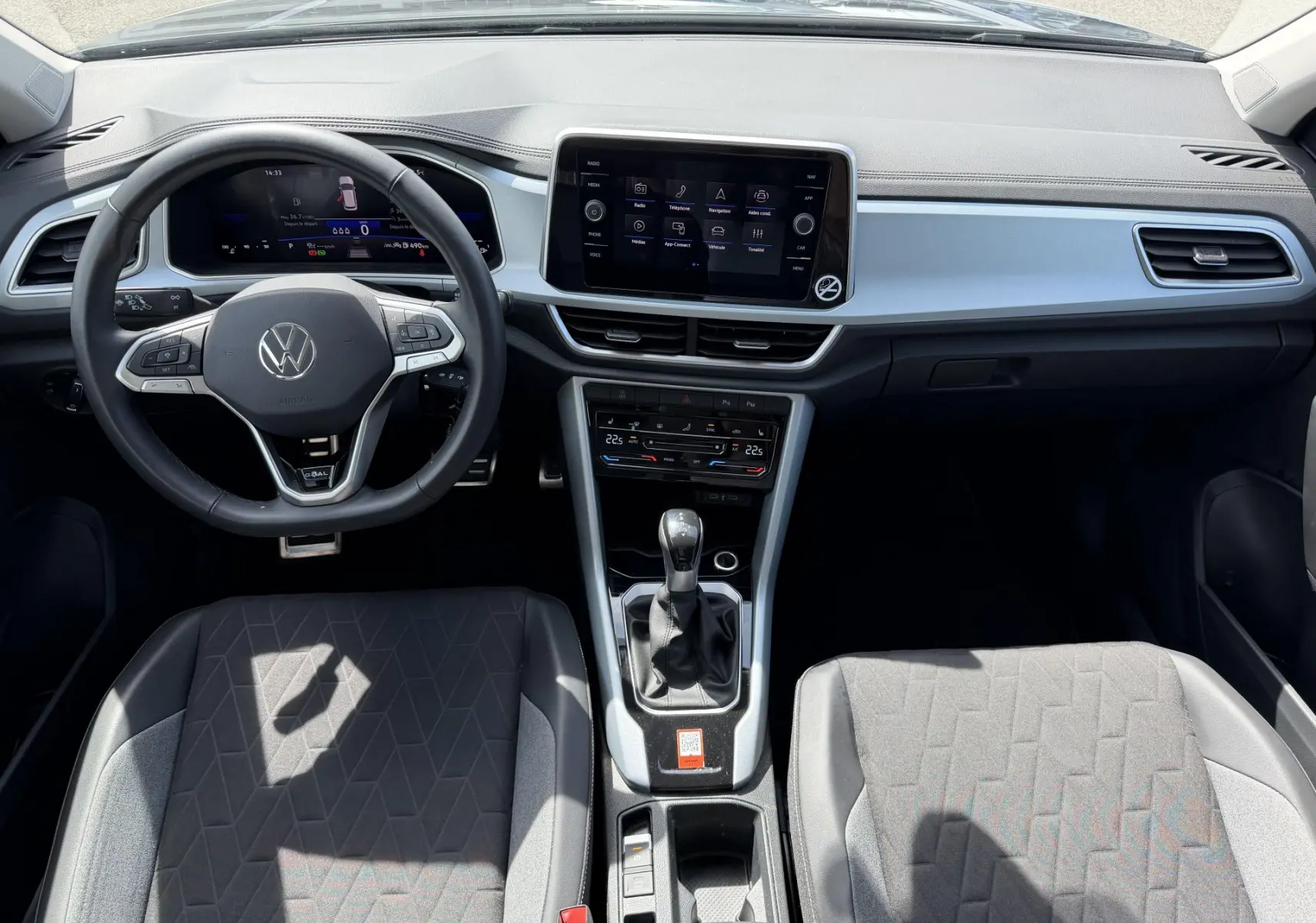 Vue intérieure avant du Volkswagen T-Roc 2025 avec tableau de bord moderne, volant cuir multifonction et boîte manuelle grise.
