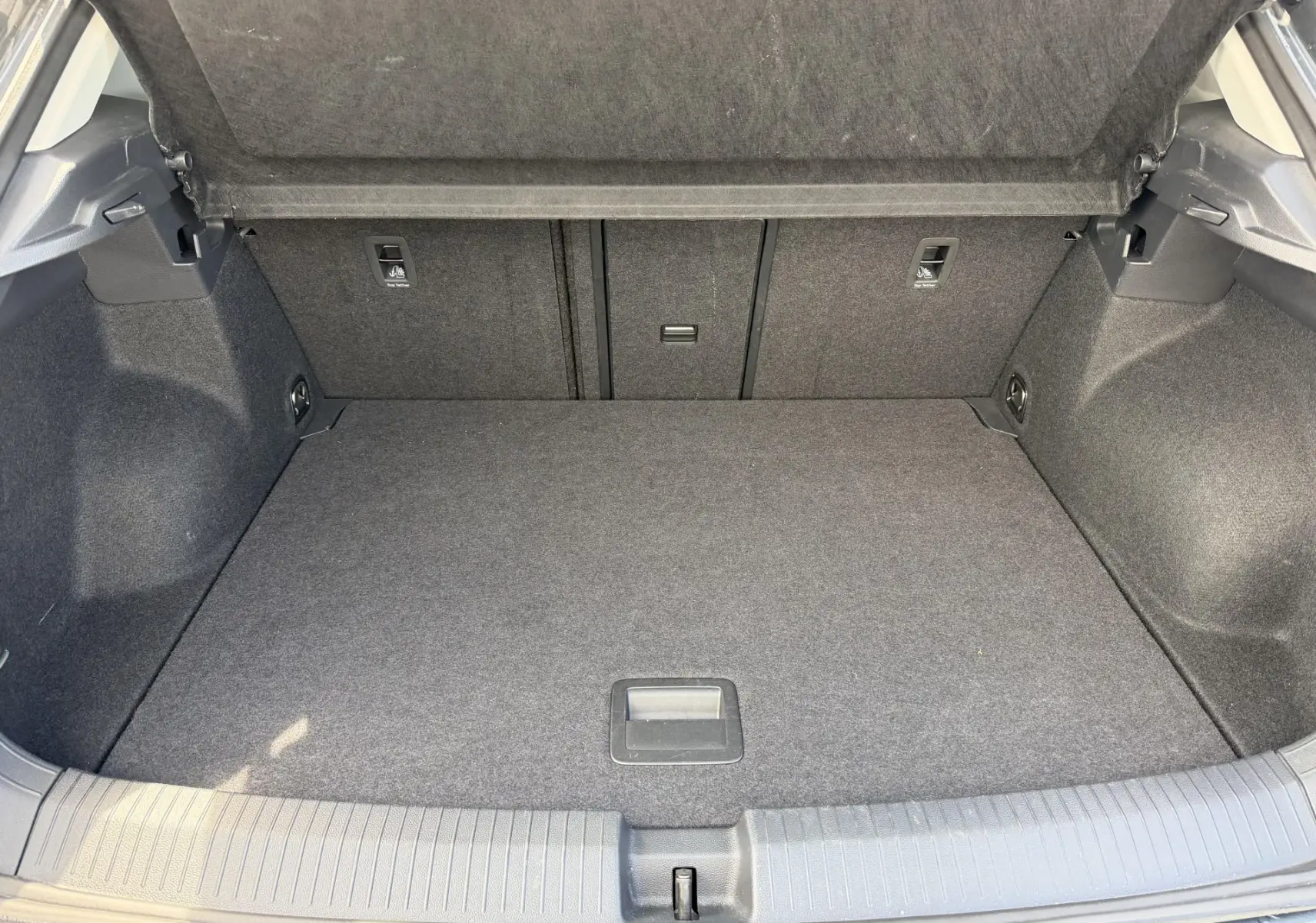 Coffre ouvert vu de face du Volkswagen T-Roc gris, montrant l'espace de chargement vide et la moquette intérieure.