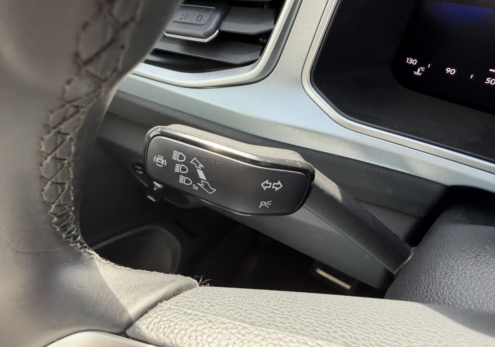 Gros plan sur la commande de clignotants et feux du Volkswagen T-Roc 2025, intérieur gris avec volant cuir noir.