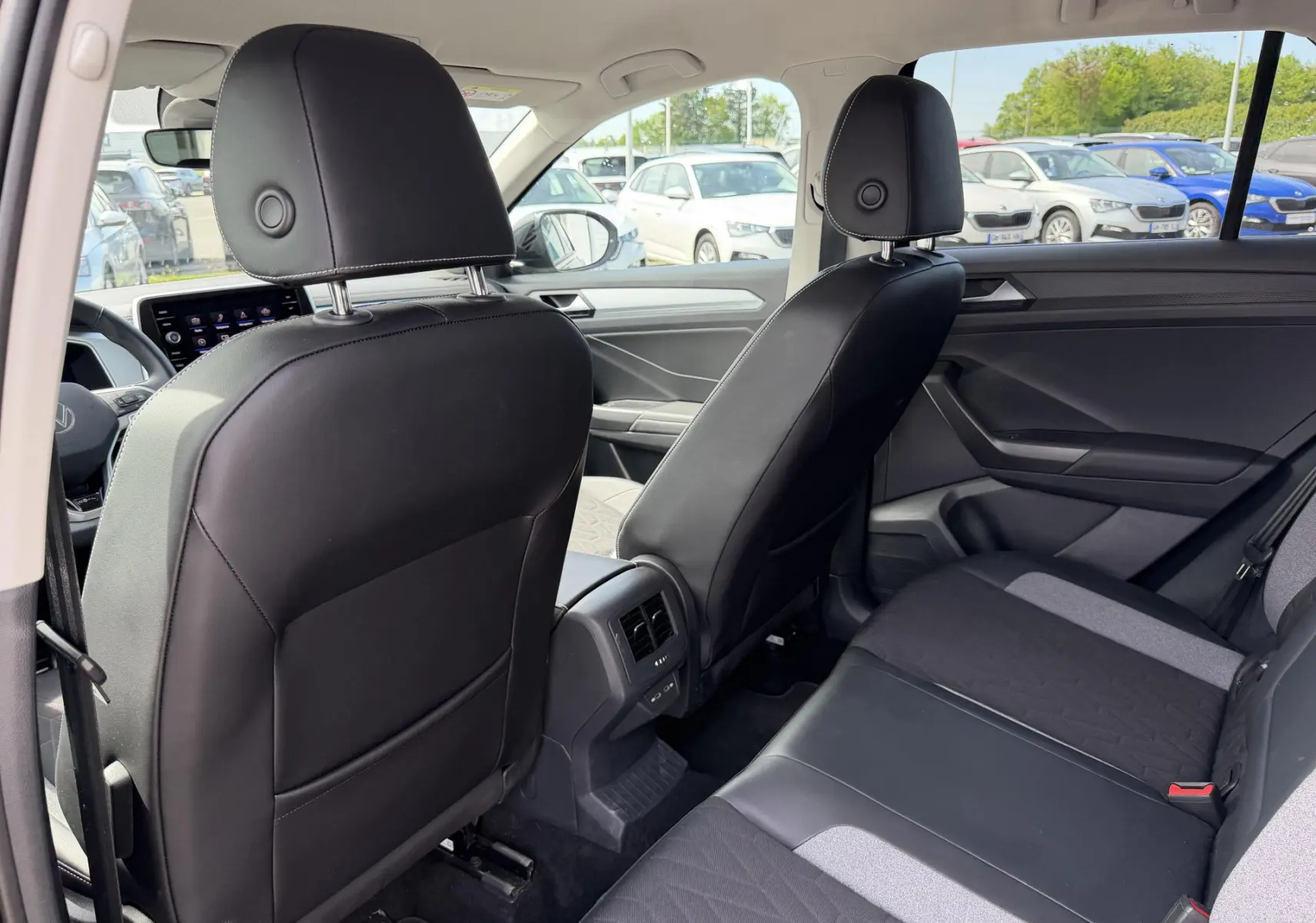 Vue intérieure arrière du Volkswagen T-Roc 2025 avec sièges noirs en cuir et tissu, et console centrale avec aérateurs.