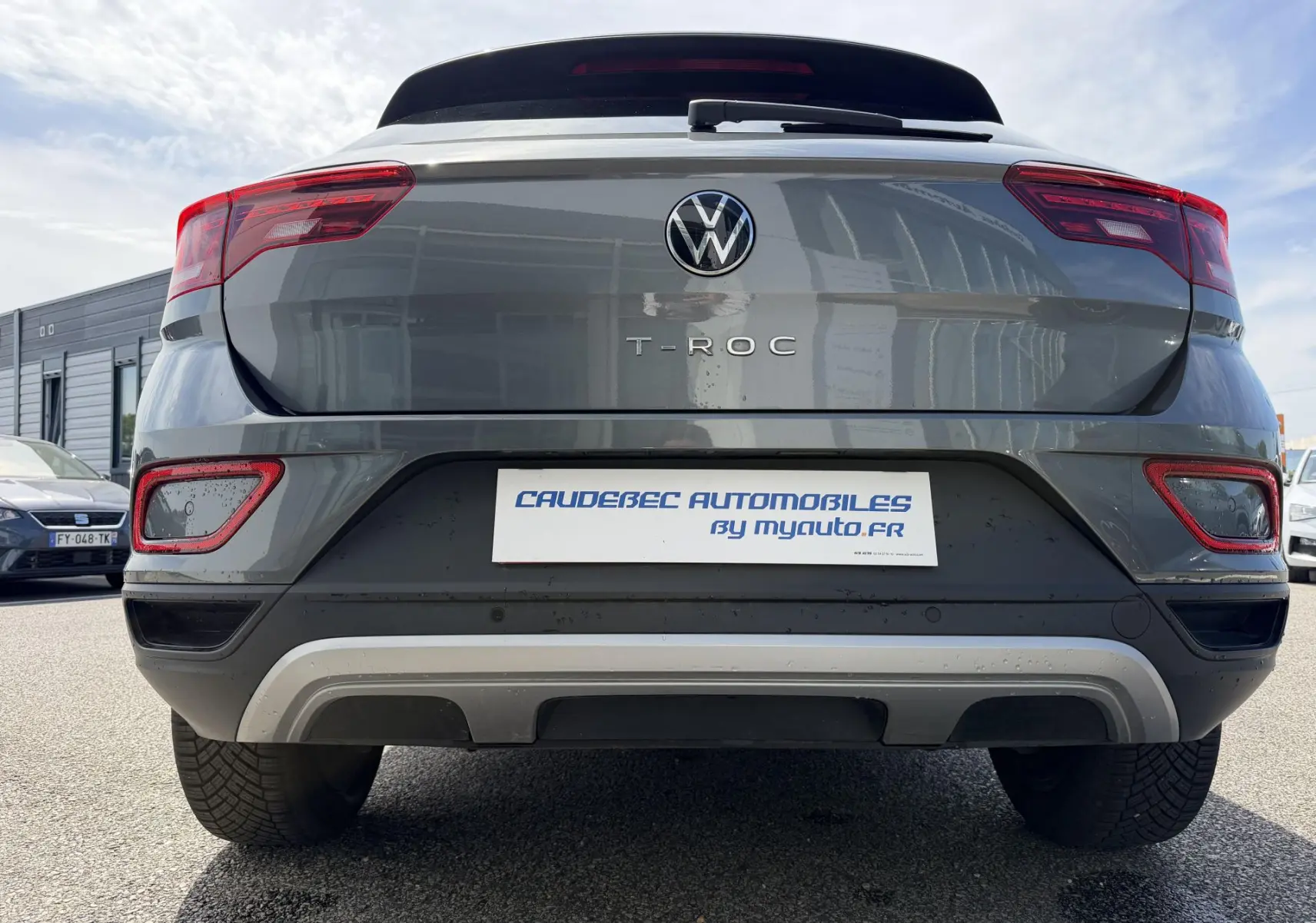 Vue arrière centrée d'un Volkswagen T-Roc gris 2025 avec feux rouges et barres de toit noires visibles.