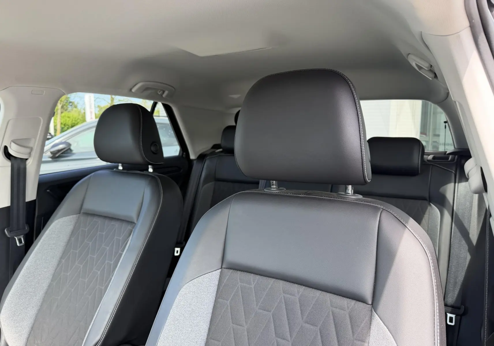 Vue intérieure des sièges avant en cuir et tissu gris du Volkswagen T-Roc, avec appuie-têtes et ceinture de sécurité visibles.