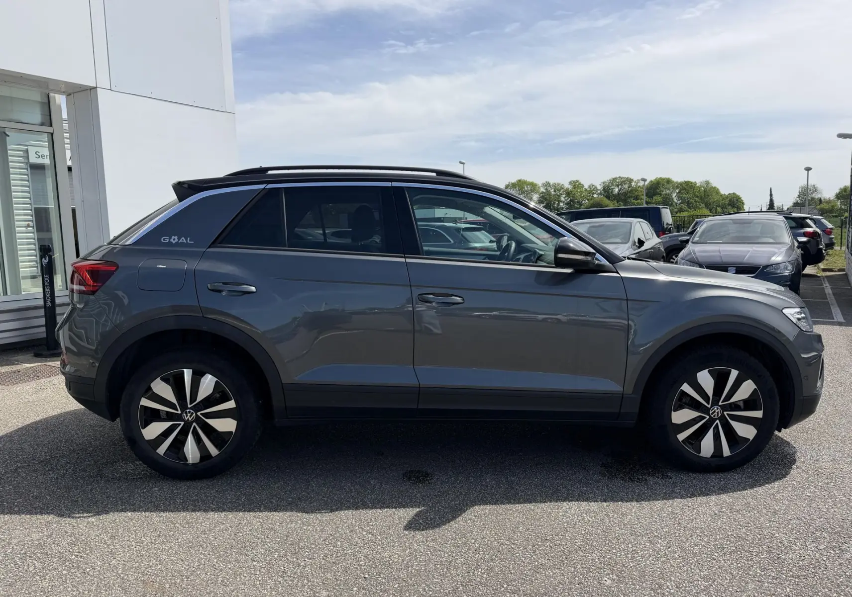 Vue latérale droite d'un Volkswagen T-Roc gris 2025 avec barres de toit noires et jantes distinctives.