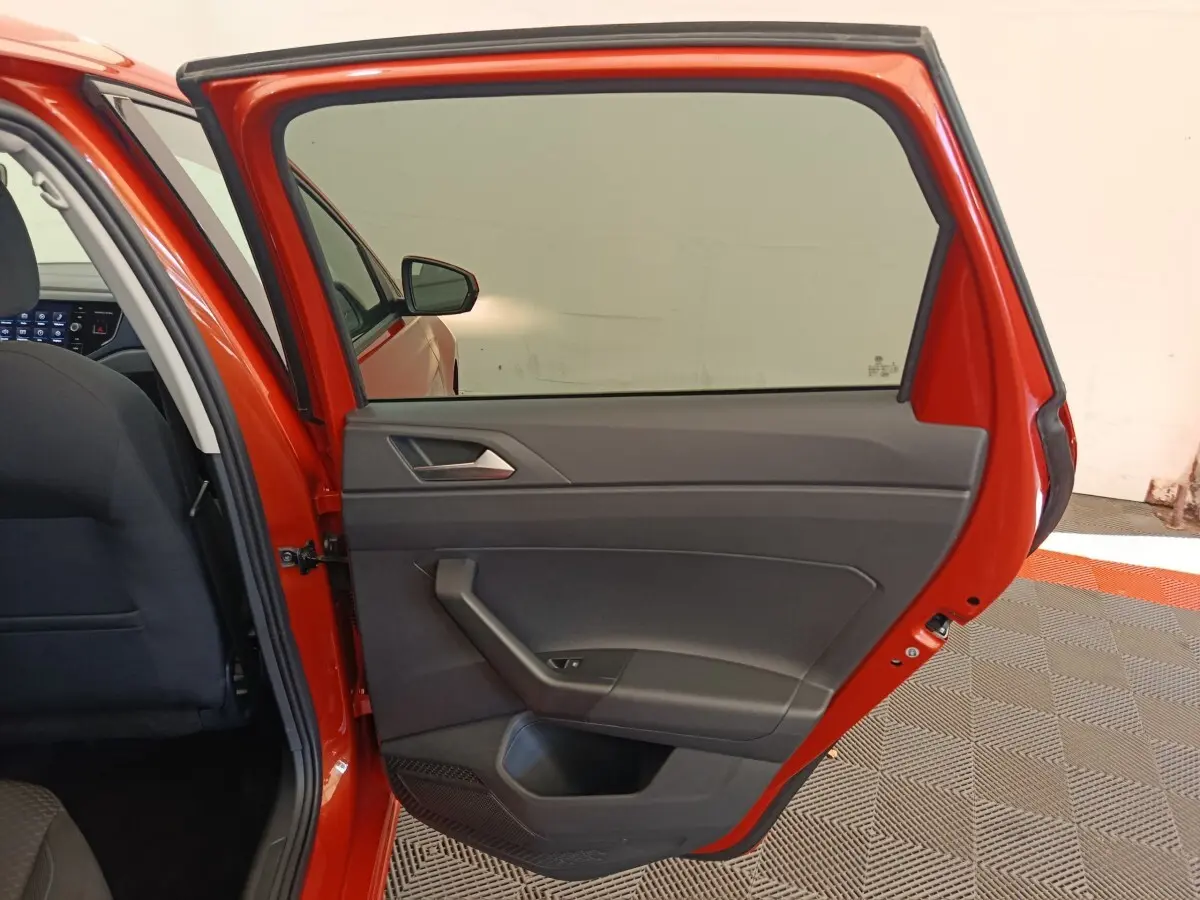 Porte arrière droite ouverte d’une Volkswagen Polo orange 2020, intérieur tissu noir et panneau de porte gris.
