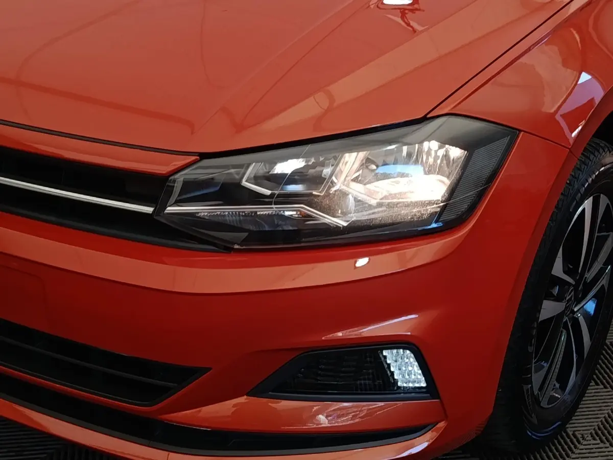 Gros plan sur l'avant droit orange vif du Volkswagen Polo 1.0 TSI 95 United avec phare LED et jante alliage noire.