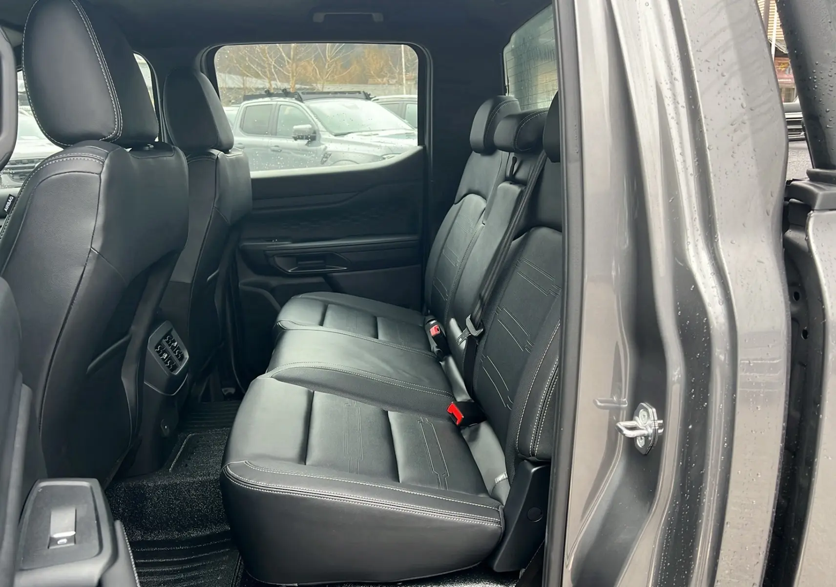 Vue côté droit arrière du Ford Ranger 2025 gris carbone, montrant les sièges arrière en cuir noir avec surpiqûres blanches.
