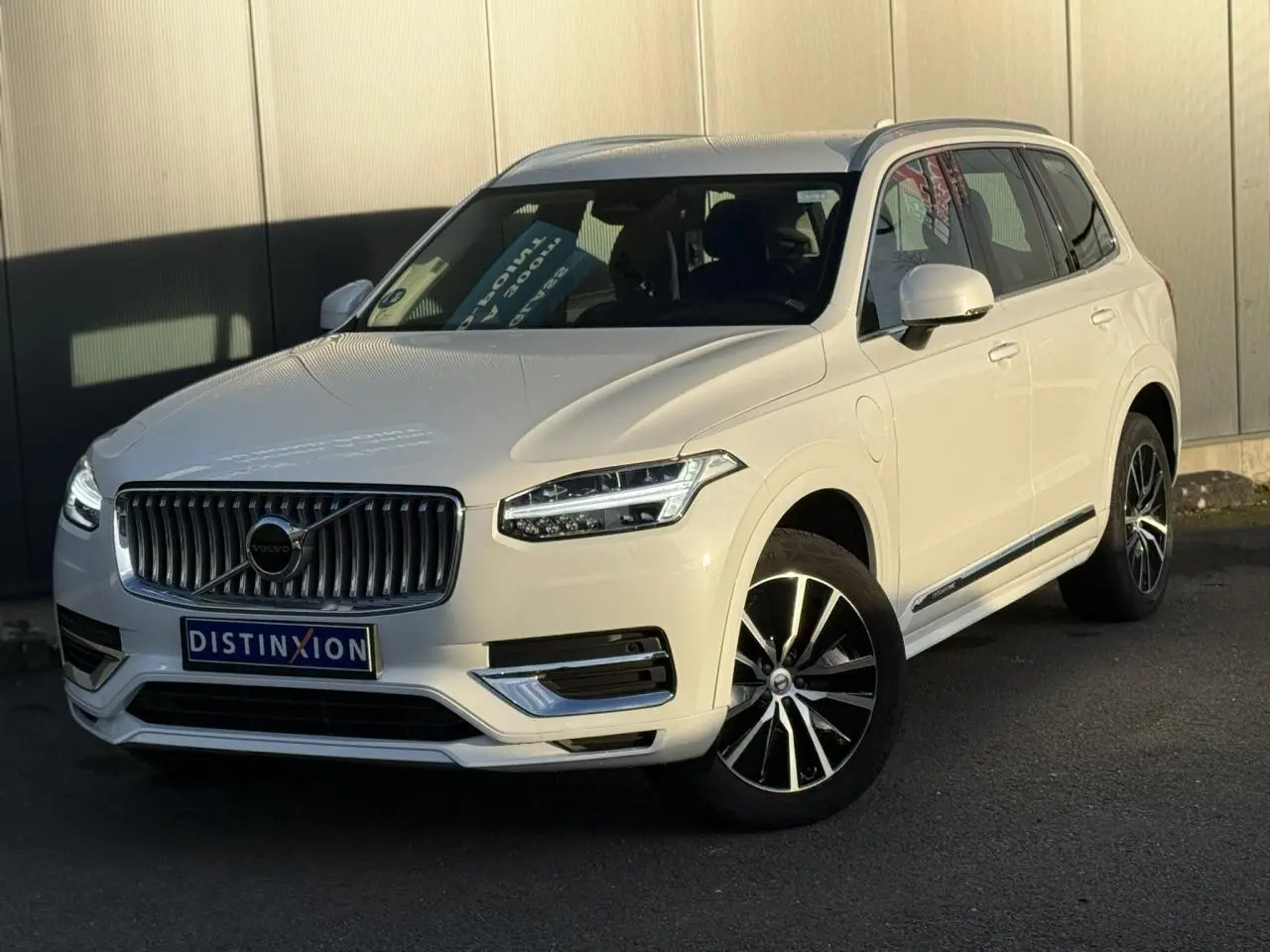 Volvo XC90 blanc Crystal en 3/4 avant droit, avec jantes alliage noires et contours chromés visibles.