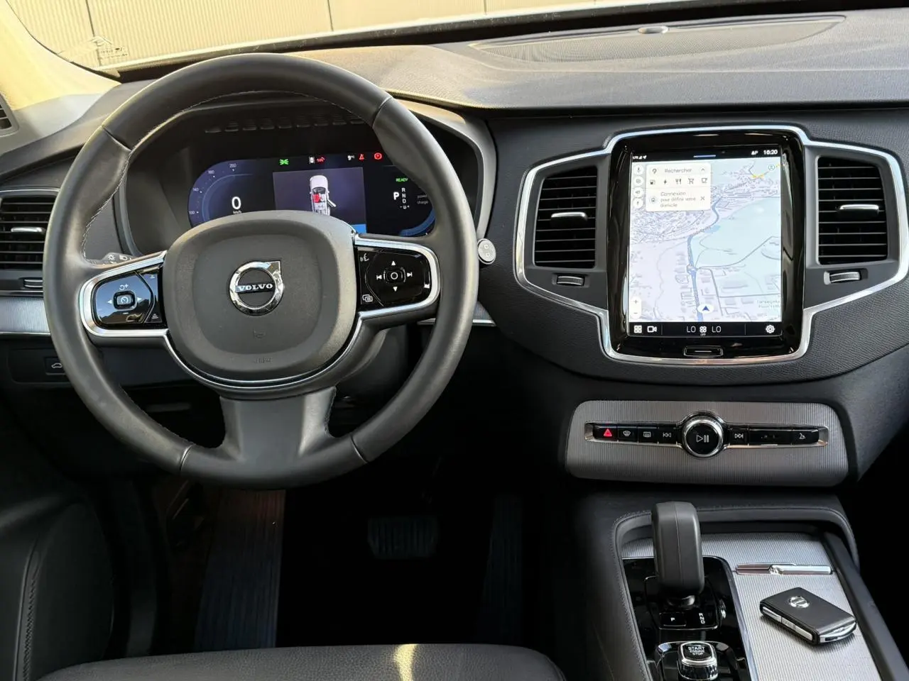 Vue de face de l'intérieur du Volvo XC90 blanc Crystal 2024, volant cuir et écran tactile central avec navigation.