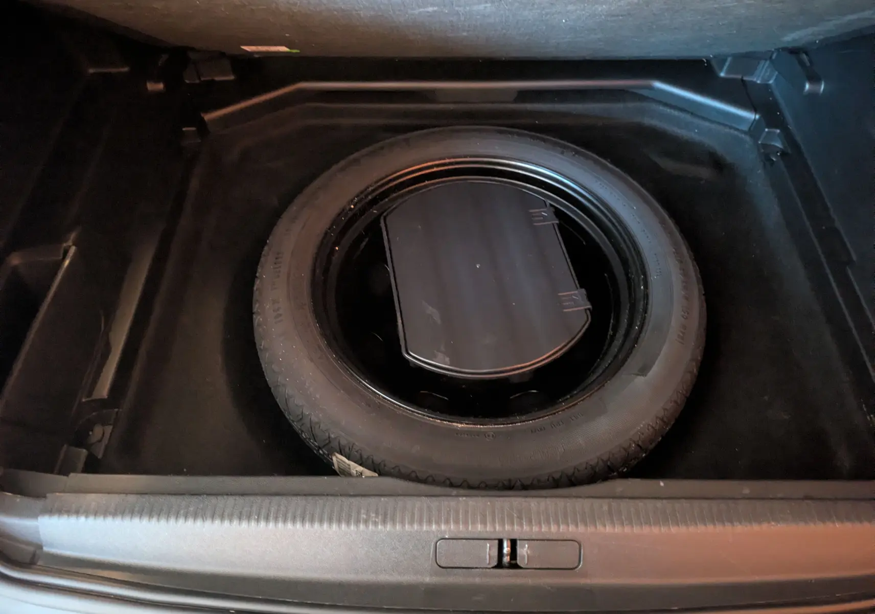 Vue plongeante sur la roue de secours noire dans le coffre d’un Peugeot 3008 gris Arthense de 2019.