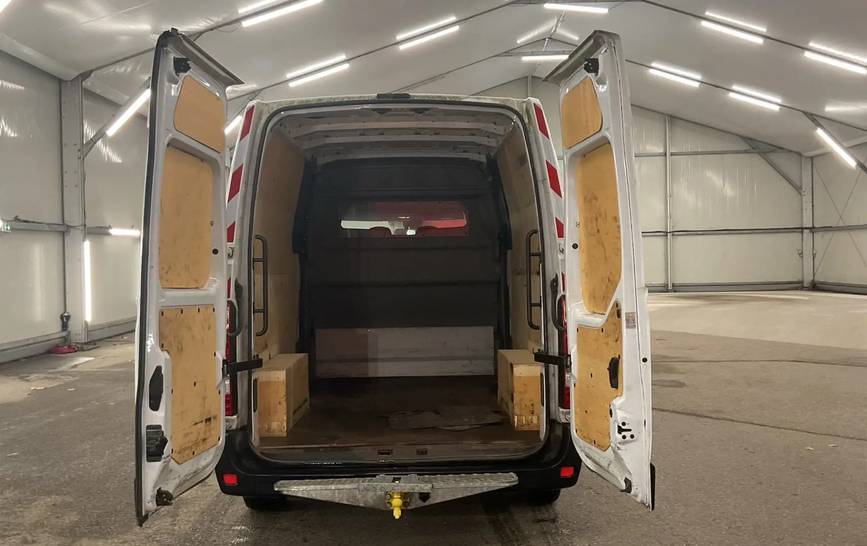 Vue arrière du Renault Master blanc avec portes arrière ouvertes, montrant l'espace de chargement boisé et un attelage.