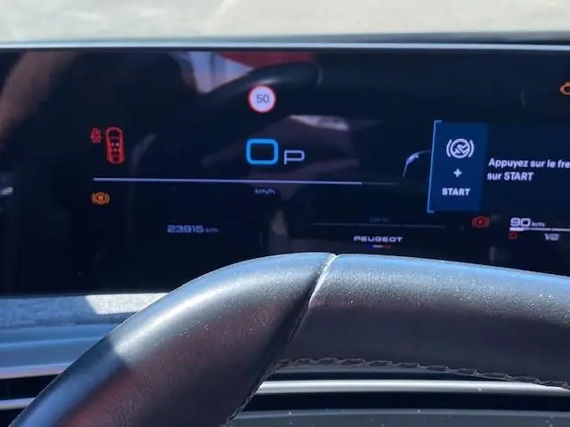 Vue rapprochée du tableau de bord numérique du Peugeot 3008 hybride 2024, affichant la vitesse et les alertes au-dessus du volant noir.
