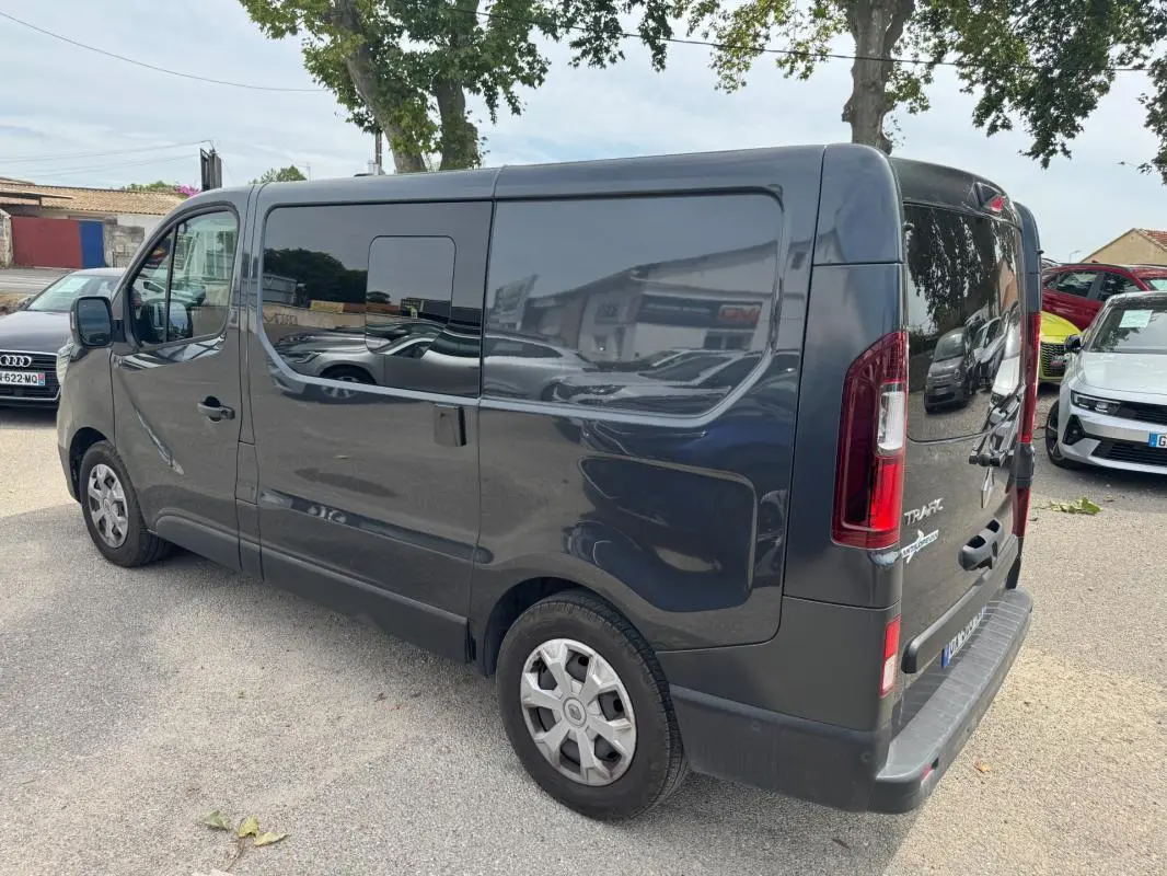 Vue 3/4 arrière droite d’un Renault Trafic Fourgon gris foncé avec vitres surteintées et porte latérale visible.