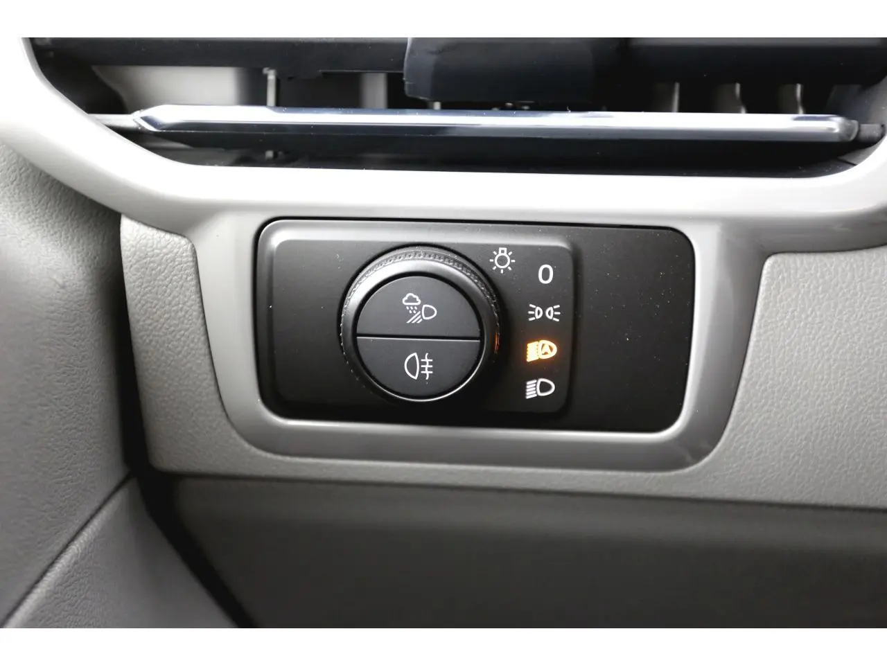 Gros plan sur la molette de commande des phares du Volkswagen Transporter T7 Business, intérieur gris clair.