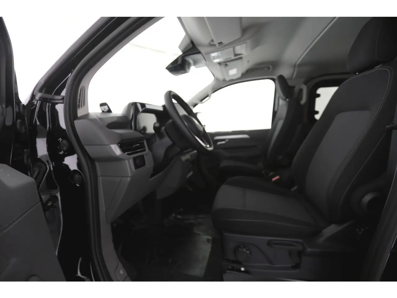 Vue intérieure côté gauche du Volkswagen Transporter T7 2025, montrant sièges noirs et tableau de bord moderne.