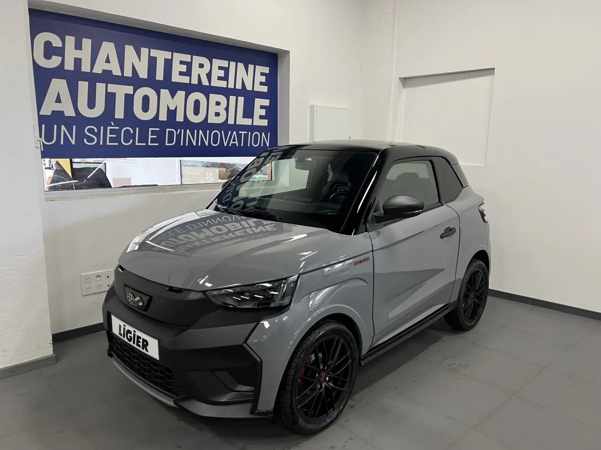 Vue 3/4 avant droite d'une Ligier JS50 gris clair avec toit noir et jantes noires en showroom.