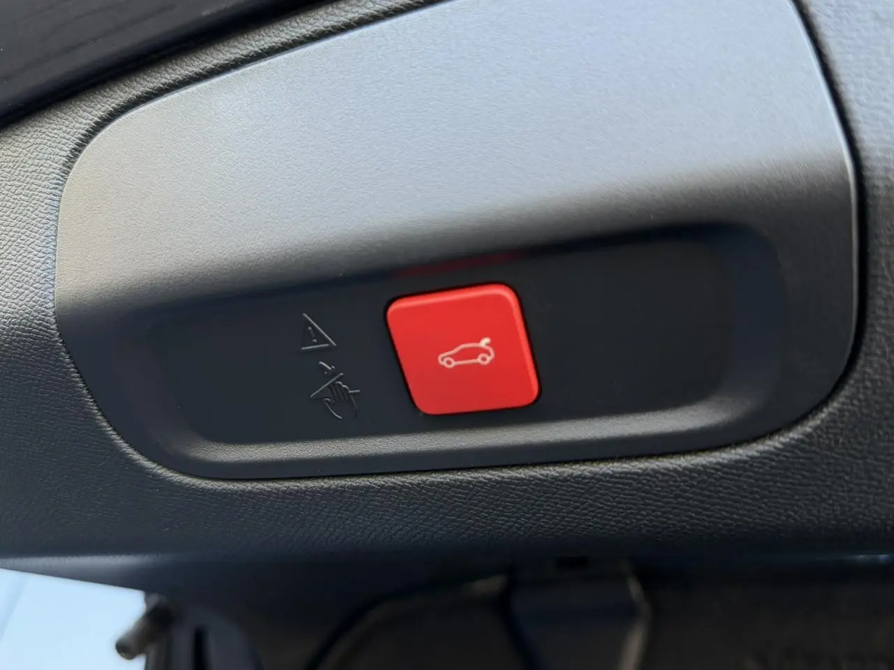 Gros plan sur le bouton rouge d'ouverture du hayon dans l'habitacle noir du Peugeot 408 Hybrid blanc Okenite.