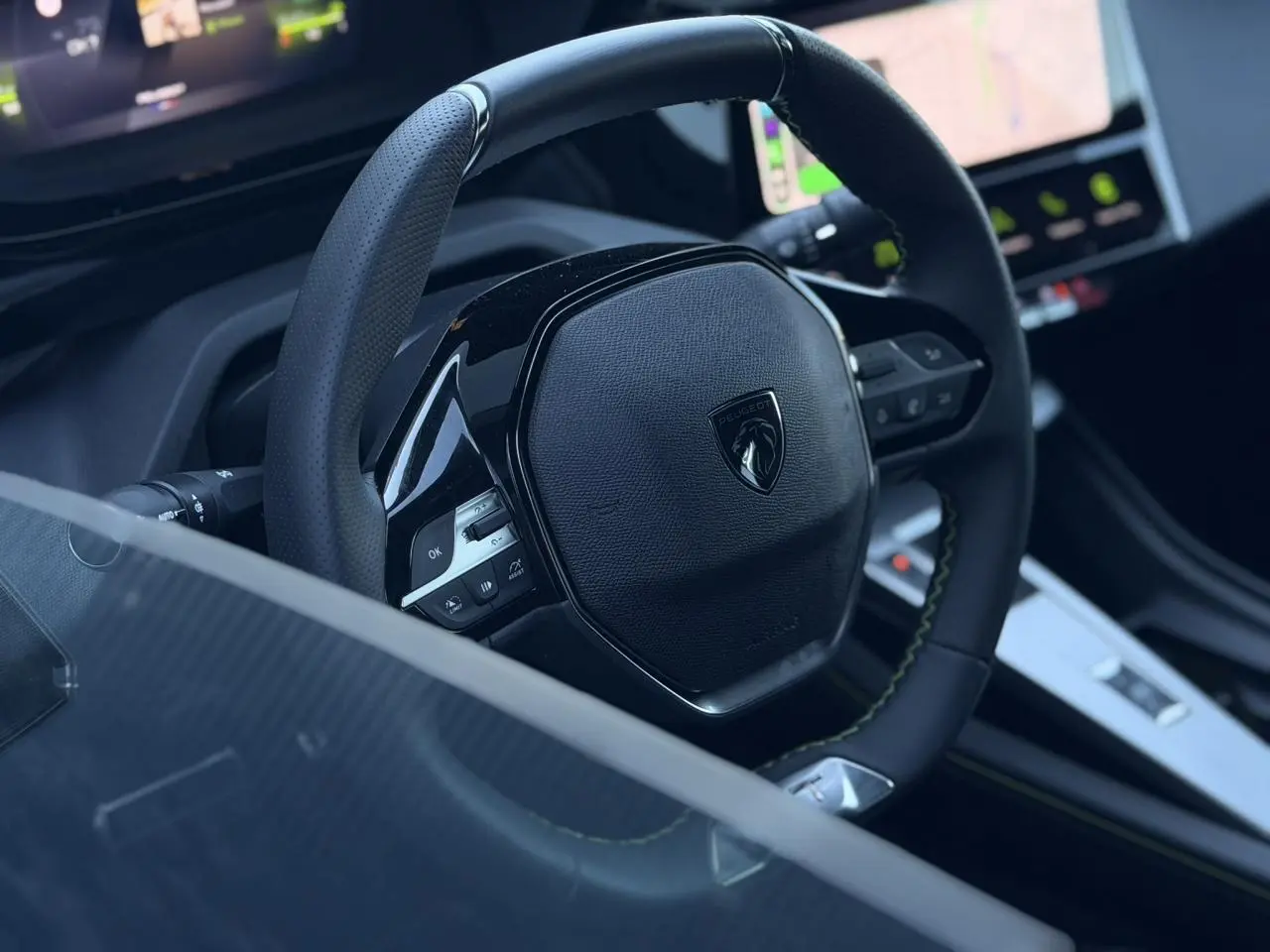 Gros plan sur le volant cuir perforé noir avec logo Peugeot, tableau de bord numérique et console centrale du Peugeot 408 Hybrid 2025.