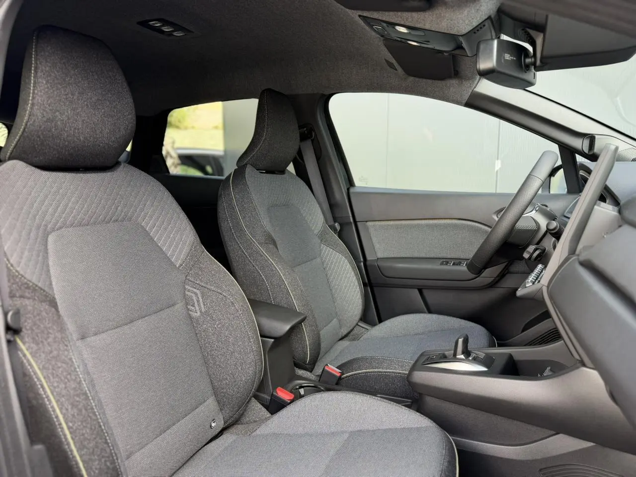 Vue intérieure côté droit du Renault Captur 2026, montrant les sièges tissu gris avec coutures contrastées et console centrale.