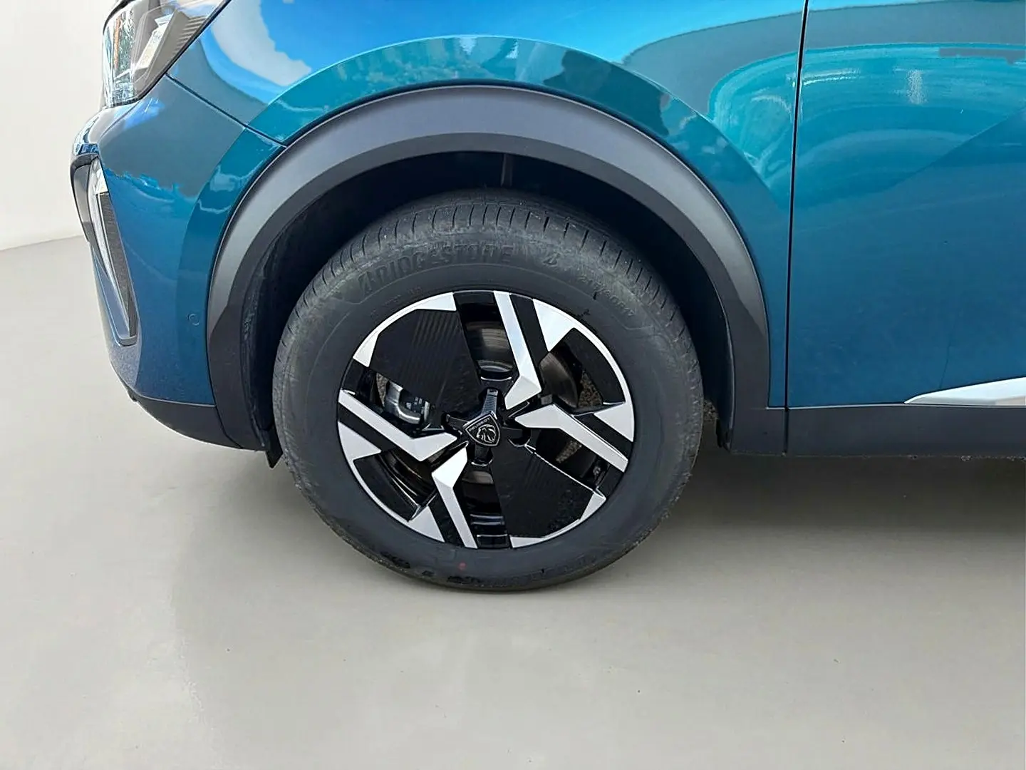 Gros plan sur la roue avant gauche d’un Peugeot 2008 bleu obsession avec jante alu au design moderne.