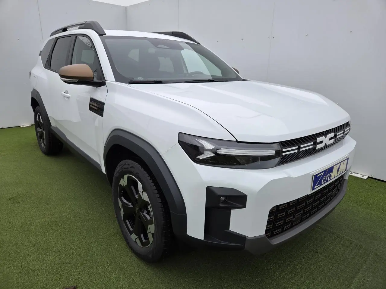 Vue 3/4 avant droit du Dacia Bigster blanc glacier avec calandre et rétroviseurs brun cuivré et jantes noires.