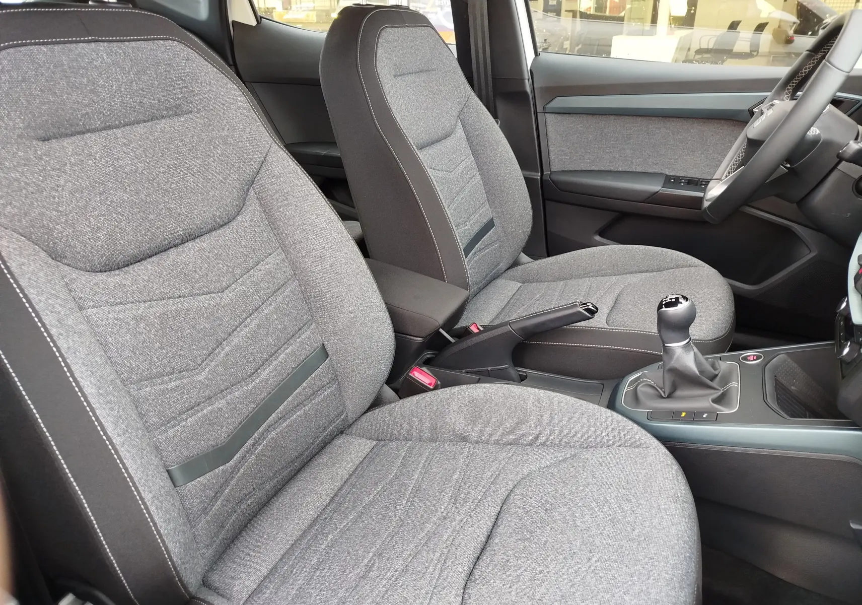 Vue intérieure côté conducteur de la SEAT Arona 2023, sièges tissu gris clair et levier de vitesses manuel.