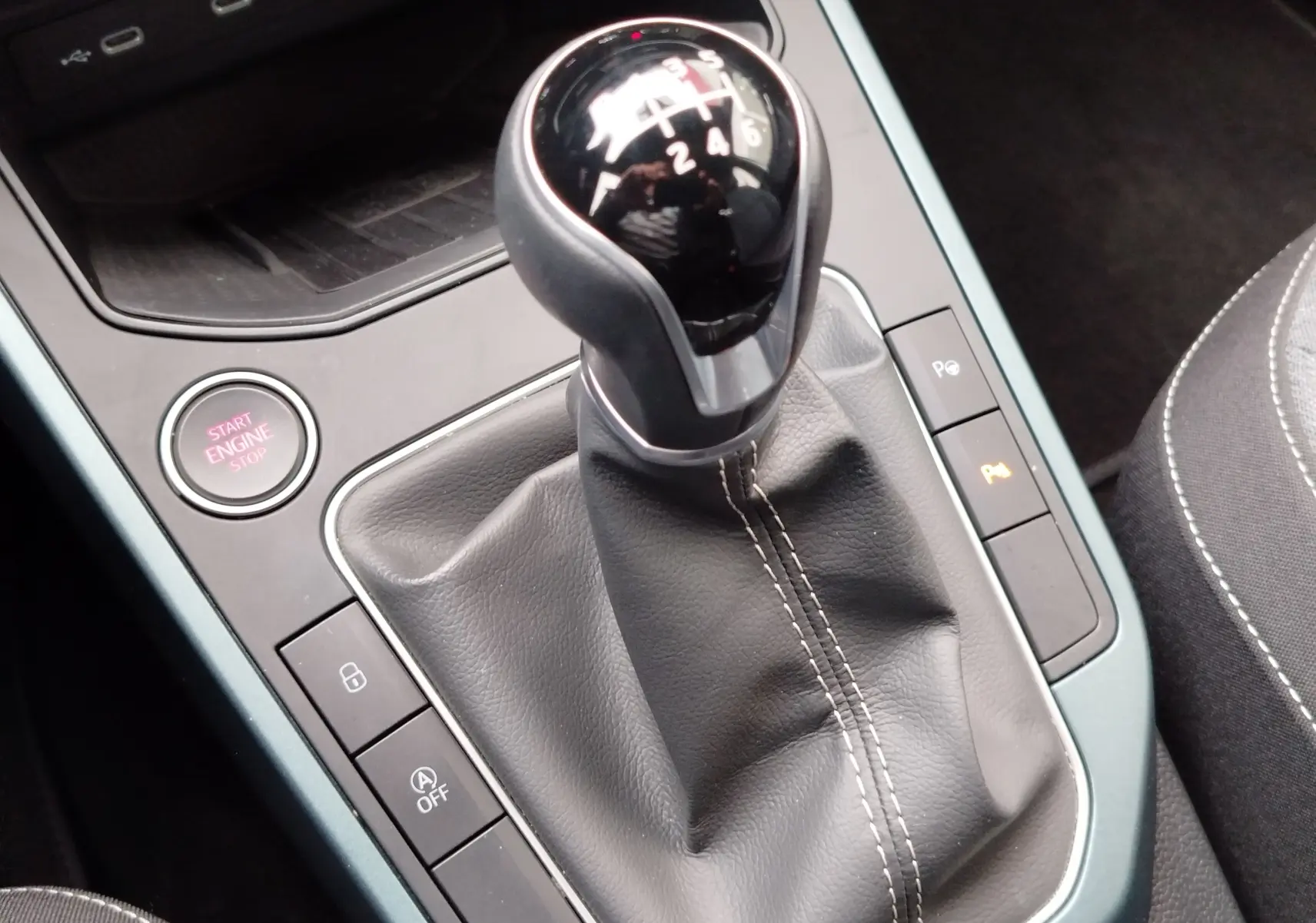 Le levier de vitesses manuel noir avec coutures blanches dans l'habitacle d'une SEAT Arona blanc Candy 2023.