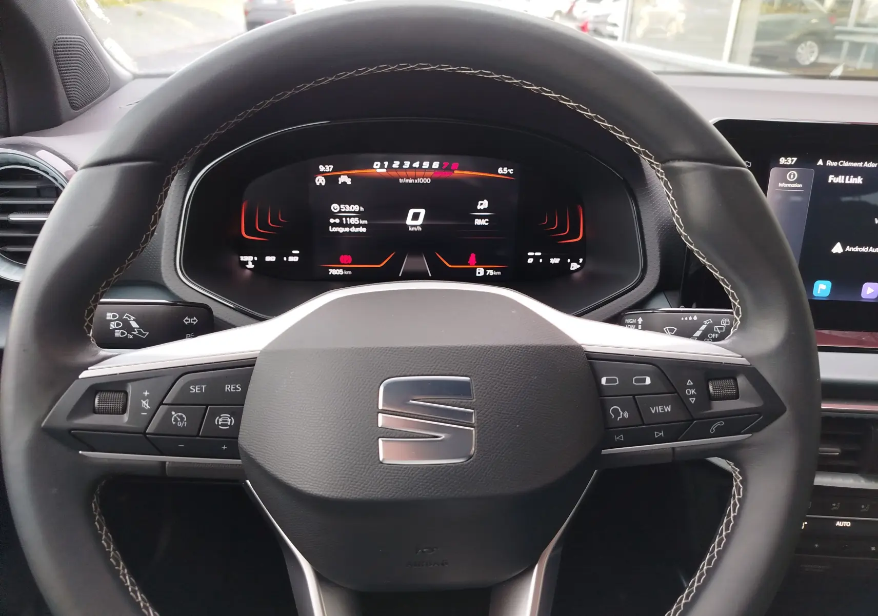 Vue rapprochée du volant multifonction noir avec coutures blanches et tableau de bord numérique du SEAT Arona 2023.