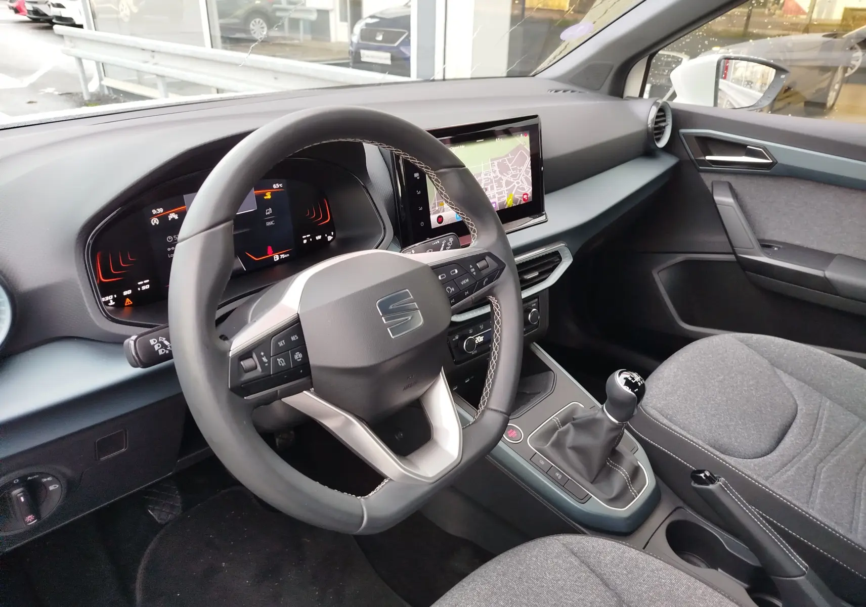 Vue intérieure côté conducteur du tableau de bord et volant du SEAT Arona blanc avec écran tactile et levier de vitesses manuel.