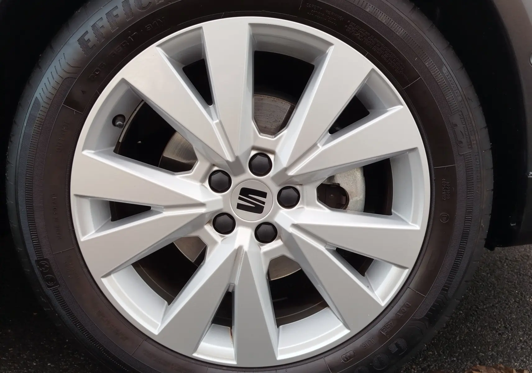 Gros plan sur la jante argentée avec logo SEAT, montée sur un pneu Goodyear, sur un SEAT Arona blanc.