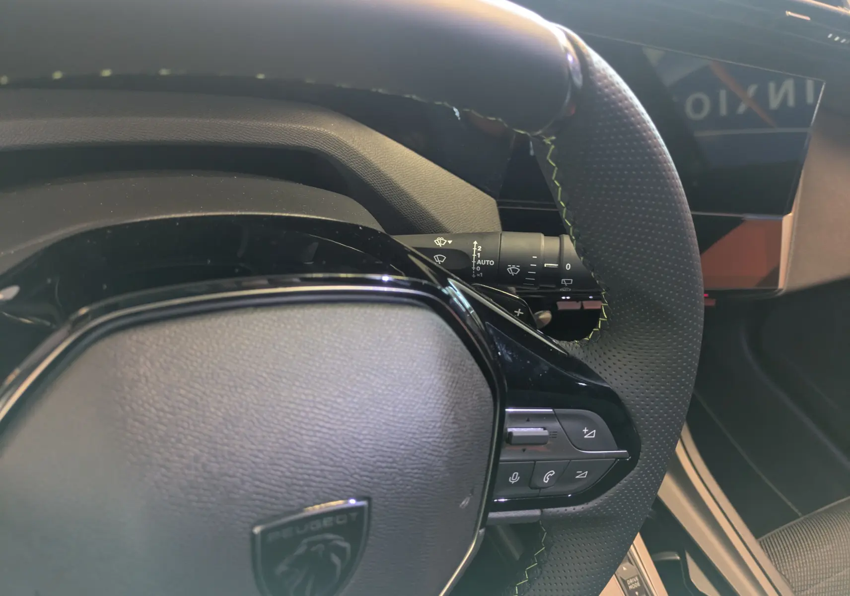 Gros plan sur le volant perforé avec surpiqûres vertes du Peugeot 308 Hybrid 145 e-DCS6 GT, tableau de bord partiel visible.