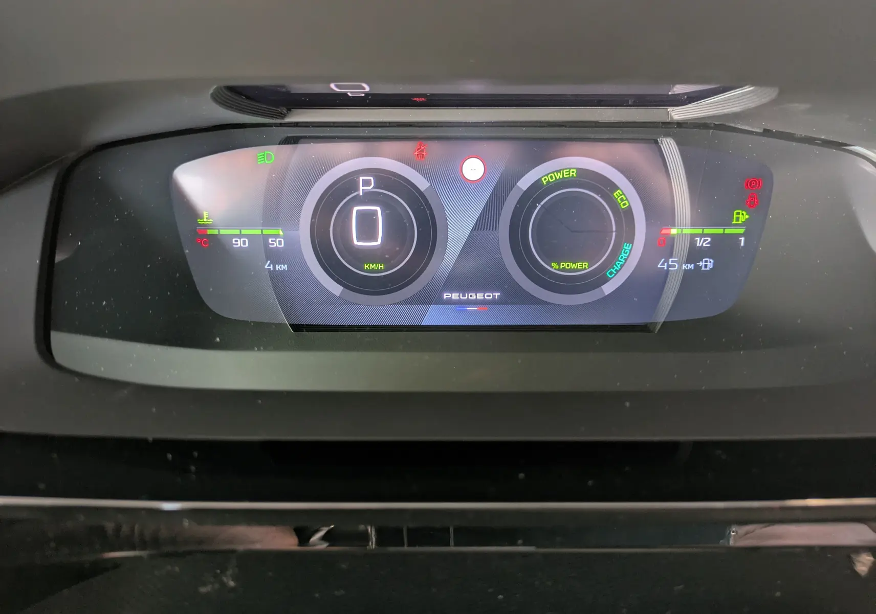 Tableau de bord numérique du Peugeot 308 Hybrid 145 en vue frontale, affichant la vitesse, la puissance et les indicateurs de charge.
