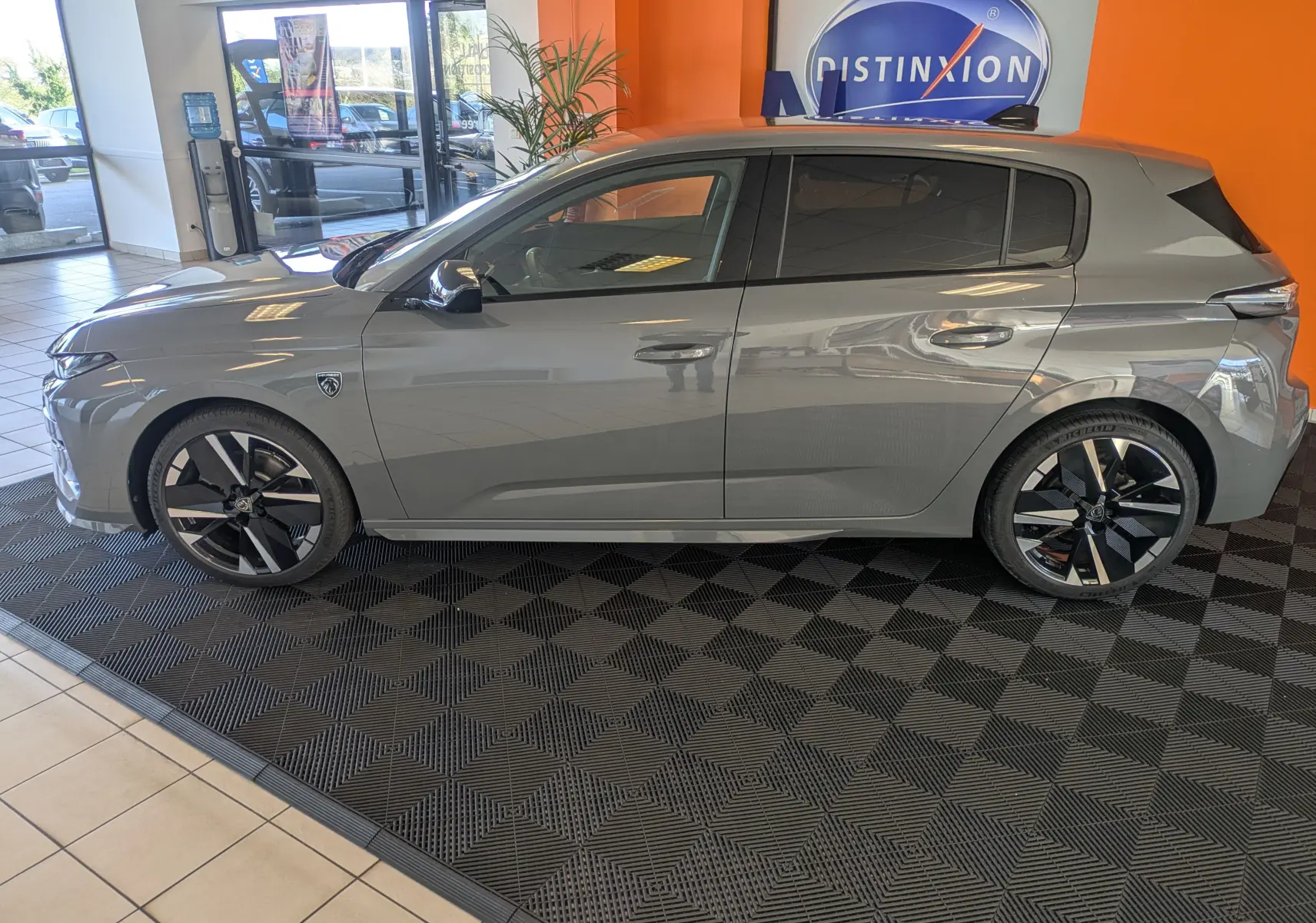 Profil côté gauche du Peugeot 308 gris selenium hybride 2026 en intérieur, soulignant ses jantes noires et détails modernes.