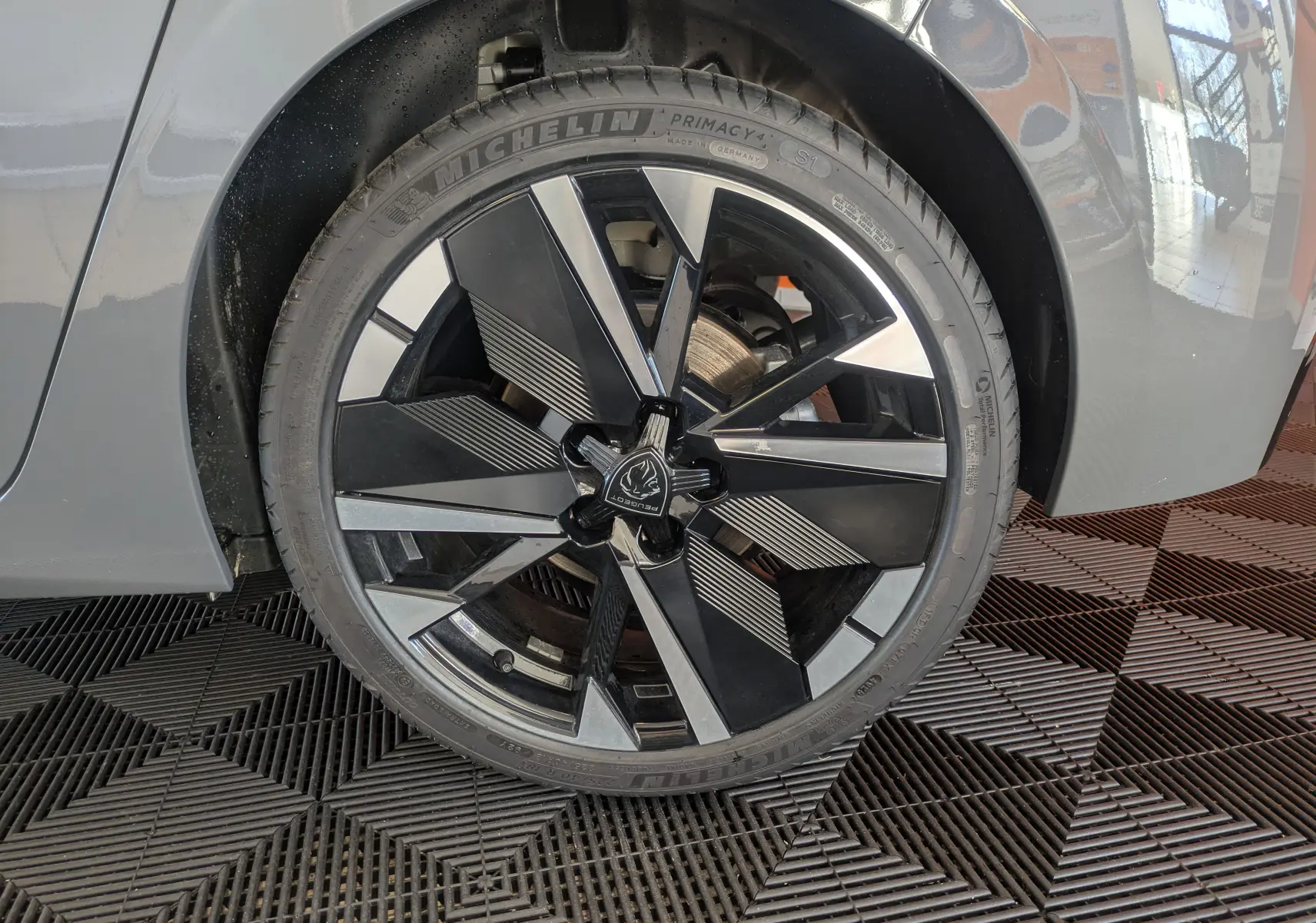 Gros plan sur la roue avant droite du Peugeot 308 gris Selenium, mettant en valeur la jante noire et argentée au design moderne.