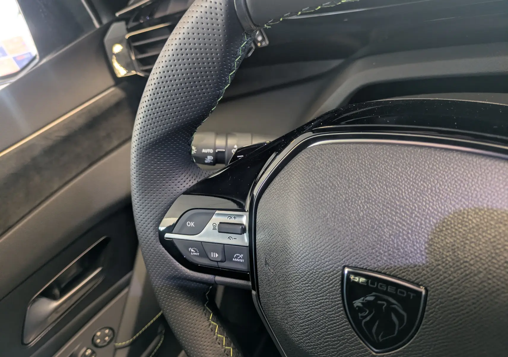 Gros plan sur le volant perforé noir avec surpiqûres vertes du Peugeot 308 hybride gris Selenium, côté gauche.