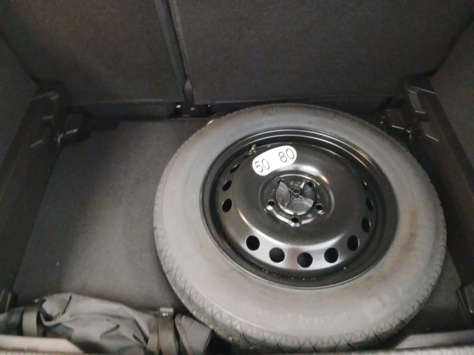 Vue du coffre du Renault Captur E-Tech Full Hybrid 2023 montrant la roue de secours noire sur fond gris cassiopée.