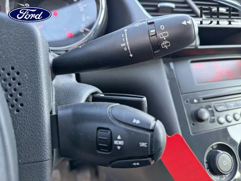 Gros plan sur les commandes au volant noir d’un Peugeot 3008 1.6 HDi112 FAP Style noir, tableau de bord en arrière-plan.