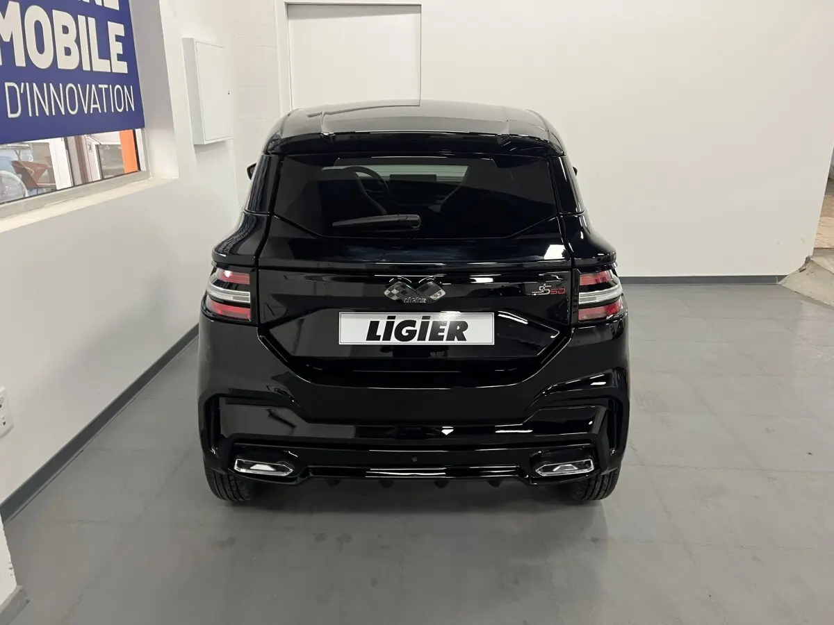 Vue arrière d'une Ligier JS50 noire 2026 avec feux LED et jantes alu noires mates dans un intérieur blanc.