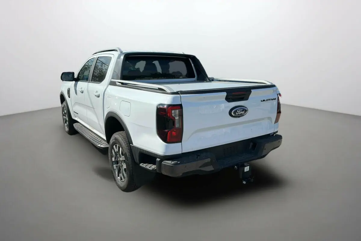 Ford Ranger blanc en 3/4 arrière droit, avec benne couverte et attelage visible.