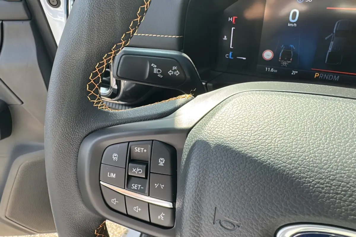 Gros plan sur le volant cuir noir avec surpiqûres orange et commandes multifonctions du Ford Ranger blanc 2026.