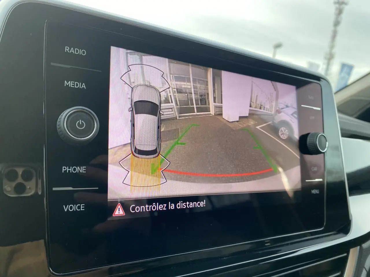 Écran tactile intérieur montrant la caméra de recul avec vue arrière et aide au stationnement du Volkswagen T-Roc gris.