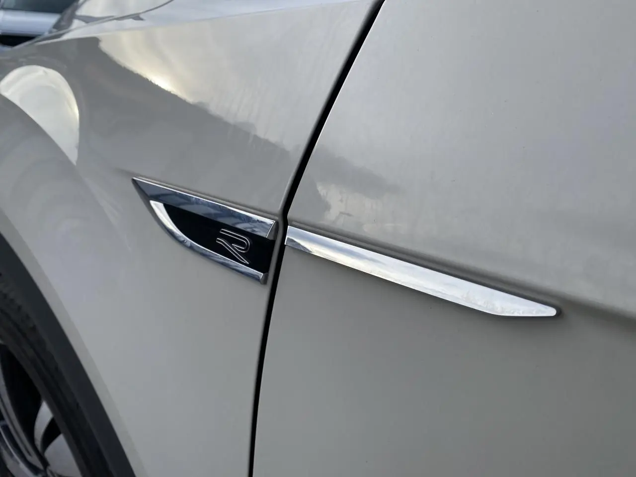 Gros plan sur l'emblème R et la baguette chromée sur l'aile avant gauche du Volkswagen T-Roc gris.